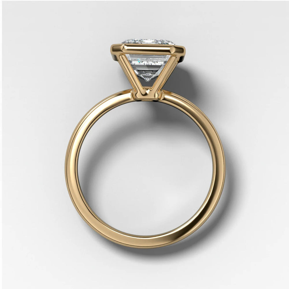 Side profile view of emerald cut diamond bezel setting in yellow gold showing open gallery for light and low profile structure