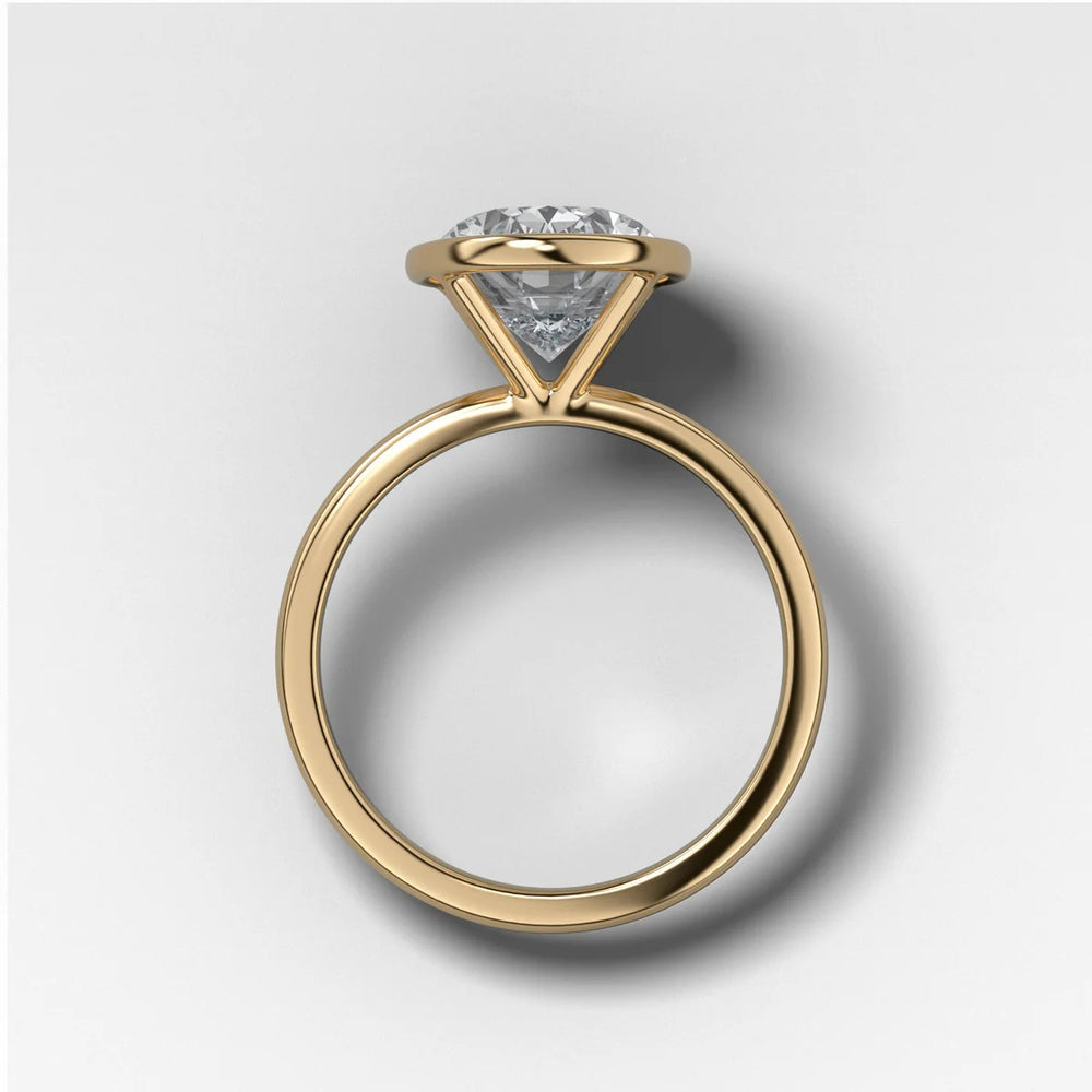 Side profile view of oval diamond bezel setting in yellow gold showing open gallery for light and low profile structure